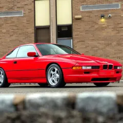Czerwone BMW serii 8 (E50) z lat 90. zaparkowane przed budynkiem z cegły.
