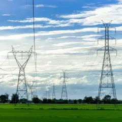 Wysokie słupy energetyczne na zielonej działce, ciągnące się w dal pod błękitnym niebem z chmurami.