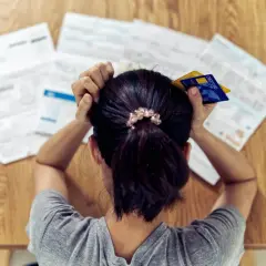Zmartwiona osoba z kartami kredytowymi w dłoniach, otoczona dokumentami. Bank nie wypłacił kredytu po akcie notarialnym, co powoduje stres.