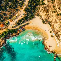 Widok z lotu ptaka na piaszczystą plażę z turkusową wodą i klifami. Idealne miejsce, by pomyśleć, co zabrać na Cypr: strój kąpielowy i krem z filtrem!