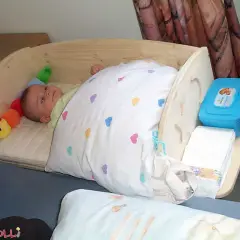 Ein süßes Baby schläft in einem selbstgebauten Babybett aus Holz. Neben ihm liegt ein bunter Raupen-Greifling. Windeln und Feuchttücher sind griffbereit.