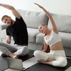 Para ćwiczy jogę w pozycji sukhasana, wykonując skłony boczne, patrząc na laptopa.