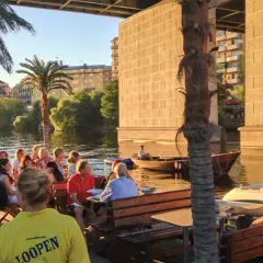 Folk njuter av kvällen vid loopen Hornstull. En båt glider förbi i vattnet.