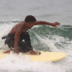 Un jeune homme surfe sur une vague à Tamraght, éclaboussant d'eau.