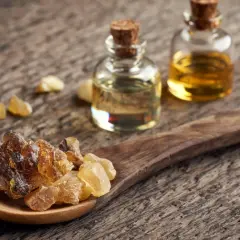 Resina di Boswellia Serrata su cucchiaio di legno, accanto a boccette di olio essenziale. Un integratore naturale.