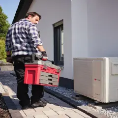 Technik z walizką narzędziową przy pompie ciepła. Regularny przegląd pompy ciepła zapewnia jej sprawność.