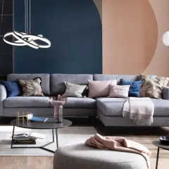 Ein hellgraues Sofa dekorieren mit Kissen in Rosa, Blau und floralen Mustern. Eine Decke liegt darüber.