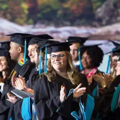 Graduates in caps and gowns applaud, celebrating their achievements in the UNC Chapel Hill online MPA program.