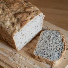 Chleb z lnem, świeżo upieczony, z jedną kromką obok, na drewnianej desce.