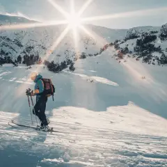 Skitouring co to? Narciarz z plecakiem wspina się po ośnieżonym stoku, słońce przebija się przez chmury, tworząc magiczną atmosferę.