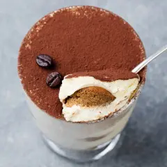 Un goloso tiramisù giallo zafferano, cosparso di cacao e chicchi di caffè, pronto per essere gustato con un cucchiaino.