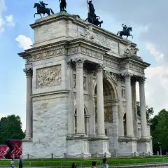 Arco di Pace a Milano, con la torre bianca sullo sfondo e un cielo nuvoloso.