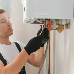 Tecnico con occhiali protettivi e guanti regola la caldaia, preoccupato per la temperatura caldaia troppo alta.