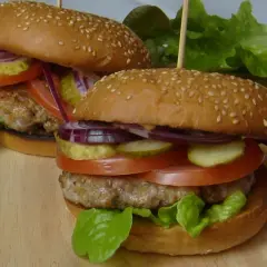Dwa soczyste burgery z bułkami do hamburgerów pysznie czy przepysznie, z pomidorami, ogórkami, cebulą i sałatą.