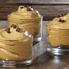Tre bicchierini di soffice crema di caffè con caffè solubile, guarniti con chicchi di caffè, su un tavolo di legno.