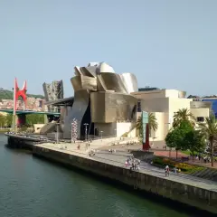 Museo Guggenheim y puente rojo, ideal para saber qué ver en Bilbao en 1 día. Paseo junto a la ría con gente disfrutando del sol.