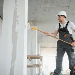 Budowlaniec maluje ścianę wałkiem. Szacowany koszt malowania domu 120m2.