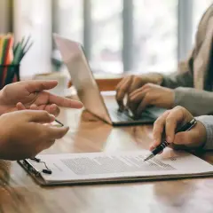 Ludzie przy stole omawiają dokumenty, jeden pisze na laptopie.