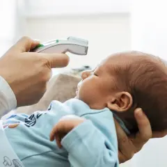 Dziecko w niebieskim ubranku, u którego rodzic mierzy temperaturę. Czyżby gorączka u niemowlaka?