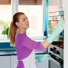 Kobieta w fartuchu i rękawiczkach czyści piekarnik. Soda oczyszczona na co pomaga? W kuchni, do czyszczenia!