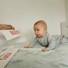 Zaciekawione niemowlę na brzuchu patrzy na kartki z napisami "Mama" i "Tata".