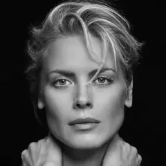 Synnøve Macody Lund, mit ihrem markanten Blick und den Händen am Hals, posiert in einem dramatischen Schwarz-Weiß-Porträt.