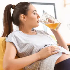 Kobieta w ciąży pije piwo bezalkoholowe z dużego kufla, relaksując się na kanapie.