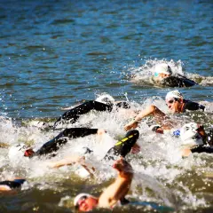 Zawodnicy walczą o pozycję podczas pływania na dystansie 1/2 ironman. Woda wzburzona, widać kaski i okulary.