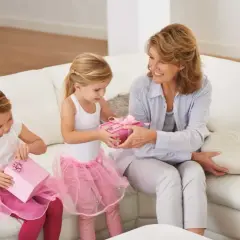 Dwie dziewczynki w różowych spódniczkach wręczają babci prezenty. To wspaniały prezent dla dziecka zamiast zabawek, pełen radości i miłości.