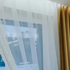 Eleganckie zasłony i firany na jednym karniszu tworzą przytulną atmosferę. Biała, ażurowa firanka i złote zasłony pięknie się komponują.