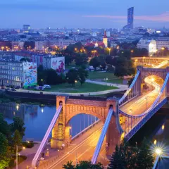 Most Wrocławia w niebieskiej godzinie w fotografii. Most Grunwaldzki i miejska panorama nocą, z rozmazanymi światłami samochodów tworzącymi smugi.