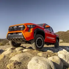 Pomarańczowa Toyota Tacoma pokonuje skalisty teren.