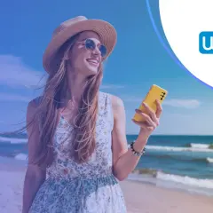 Uśmiechnięta kobieta na plaży z telefonem. Sprawdź, ile pozyczek mozna miec w Wonga, by spełnić wakacyjne marzenia.
