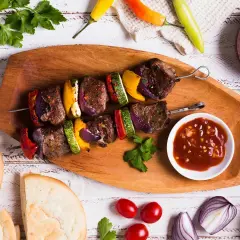 Brochette de rumsteck grillée avec poivrons, courgettes et oignons, servie avec une sauce savoureuse.