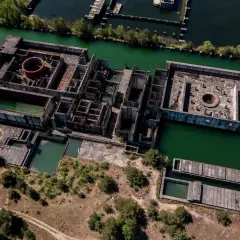 Niedokończona elektrownia atomowa Żarnowiec, z betonowymi konstrukcjami zanurzonymi w zielonej wodzie, otoczona drzewami i dziką roślinnością.