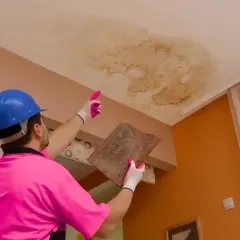 Un trabajador con casco azul y polo rosa señala una mancha de humedad en el techo, indicando que se puede caer el techo por una gotera.