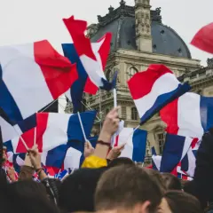 Tłum ludzi trzyma flagi francuskie. Widać charakterystyczne biało-niebiesko-czerwone pasy, jak wygląda flaga francuska.