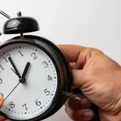 Ręka przestawia wskazówki budzika, przygotowując się na zmianę czasu na zimowy.