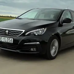 Czarny Peugeot 308 kombi z 2015 roku jedzie po drodze wśród zielonych pól.
