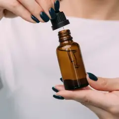 Dłonie z ciemnym lakierem do paznokci trzymają brązową buteleczkę z pipetką. Czy serum do twarzy można stosować codziennie?
