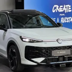 Biały Volkswagen T-Roc z czarnym dachem i felgami. Na ekranie w tle napis "CREATE LIKE A ROCSTAR". Sprawdź aktualną volkswagen t-roc cena.