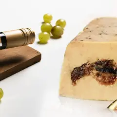 Bouteille de vin blanc à côté d'un bloc de foie gras aux figues, avec des raisins verts et des quartiers de figues. Un délice pour les amateurs d'alcool et de foie gras.