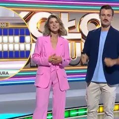 Prowadzący Koło Fortuny na tle planszy z literami i neonowych dekoracji.