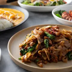 Talerz z aromatycznym makaronem tajskim, polanym sosem, z dodatkiem zielonych warzyw i czerwonych nitek chili.