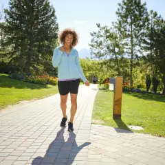 Uśmiechnięta kobieta w sportowym stroju idzie ścieżką w parku. Choć ciągle chodzę w te same miejsca, zawsze znajduję w nich coś nowego.