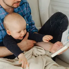 Tata czyta dziecku książeczkę. Maluch z zaciekawieniem ogląda obrazki, to jego pierwsze zdania dziecka, które słyszy.