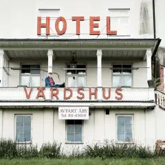 Man sitter på balkongen till ett gammalt värdshus med skylten "HOTEL VÄRDSHUS".