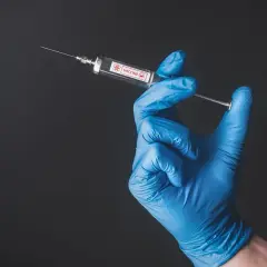Ręka w niebieskiej rękawiczce trzyma strzykawkę z napisem "VACCINE". Przygotowanie do szczepienia w Tunezji.