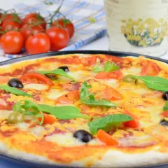 Domowa pizza z pomidorami, oliwkami i rukolą na czarnym talerzu.