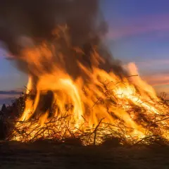 Ein riesiges Osterfeuer lodert im Abendrot. Menschen versammeln sich, um diese alte Osterfeuer Tradition zu erleben.